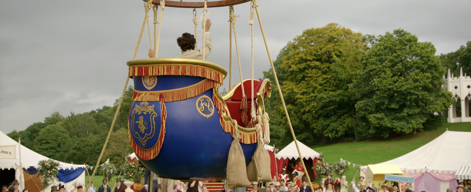 A royal blue and fringed hot air balloon in the air with a man waving at people on the ground